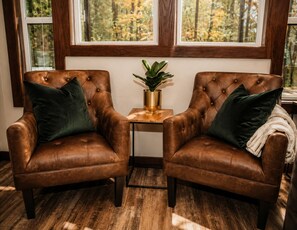 Two brown leather armchairs with green cushions, a small wooden table with a plant, and a window with a view of trees. - Adventurer at The Retreat at Water's Edge (Tracy City)