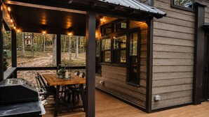 Een terras buiten met een houten tafel en stoelen, een barbecue en lichtjes.