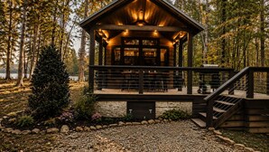 Een houten vakantiehuisje met een overdekt terras, omringd door bomen en een grindpad.