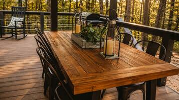 Una terraza de madera con una mesa, sillas, una parrilla y un farol.
