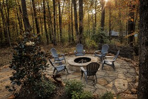 An outdoor seating area with stone flooring and Adirondack chairs around a circular stone fire pit. - Adventurer at The Retreat at Water's Edge (Tracy City)