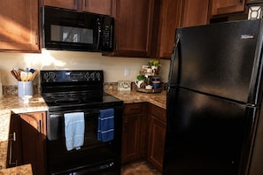 A kitchen with wooden cabinets, a black microwave, a black stove, and a black refrigerator. - Cozy Cottage at The Retreat at Deer Lick Falls (Monteagle)