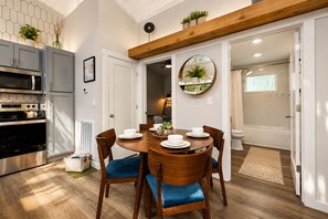 Une cuisine moderne dotée d’appareils électroménagers intégrés, un coin repas avec une table en bois et des chaises bleues, et une salle de bain visible avec une baignoire.