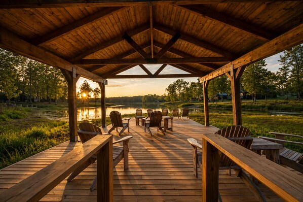Une terrasse en bois, agrémentée de chaises et de tables, qui offre une vue sur un lac et des arbres.
