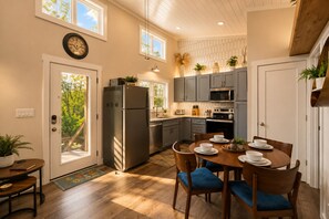 Une cuisine moderne avec des meubles gris, des appareils en acier inoxydable et un coin repas comprenant des chaises en bois et une table dressée pour quatre personnes.