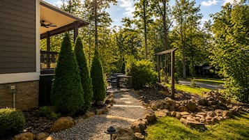 A pathway leading to a covered outdoor seating area with a pergola, surrounded by a landscaped garden with rocks and trees.