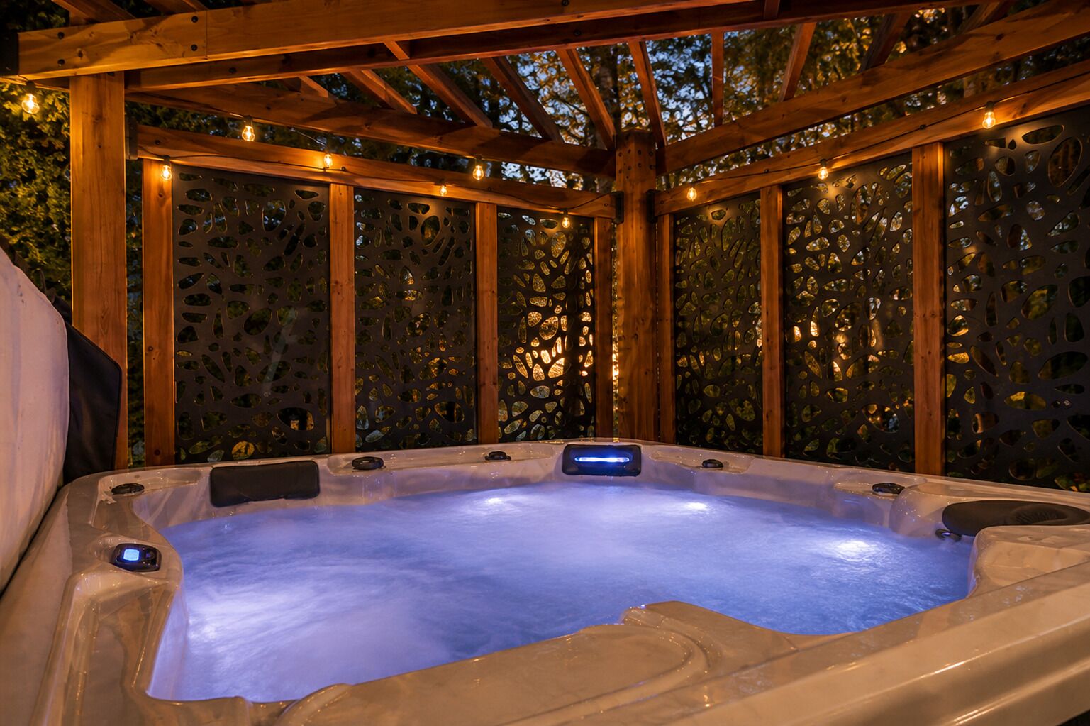 A hot tub with a wooden pergola overhead, surrounded by a decorative fence with cut-out patterns.