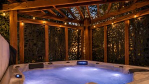 Un jacuzzi con una pérgola de madera en la parte superior, rodeado por una valla decorativa con diseños recortados.