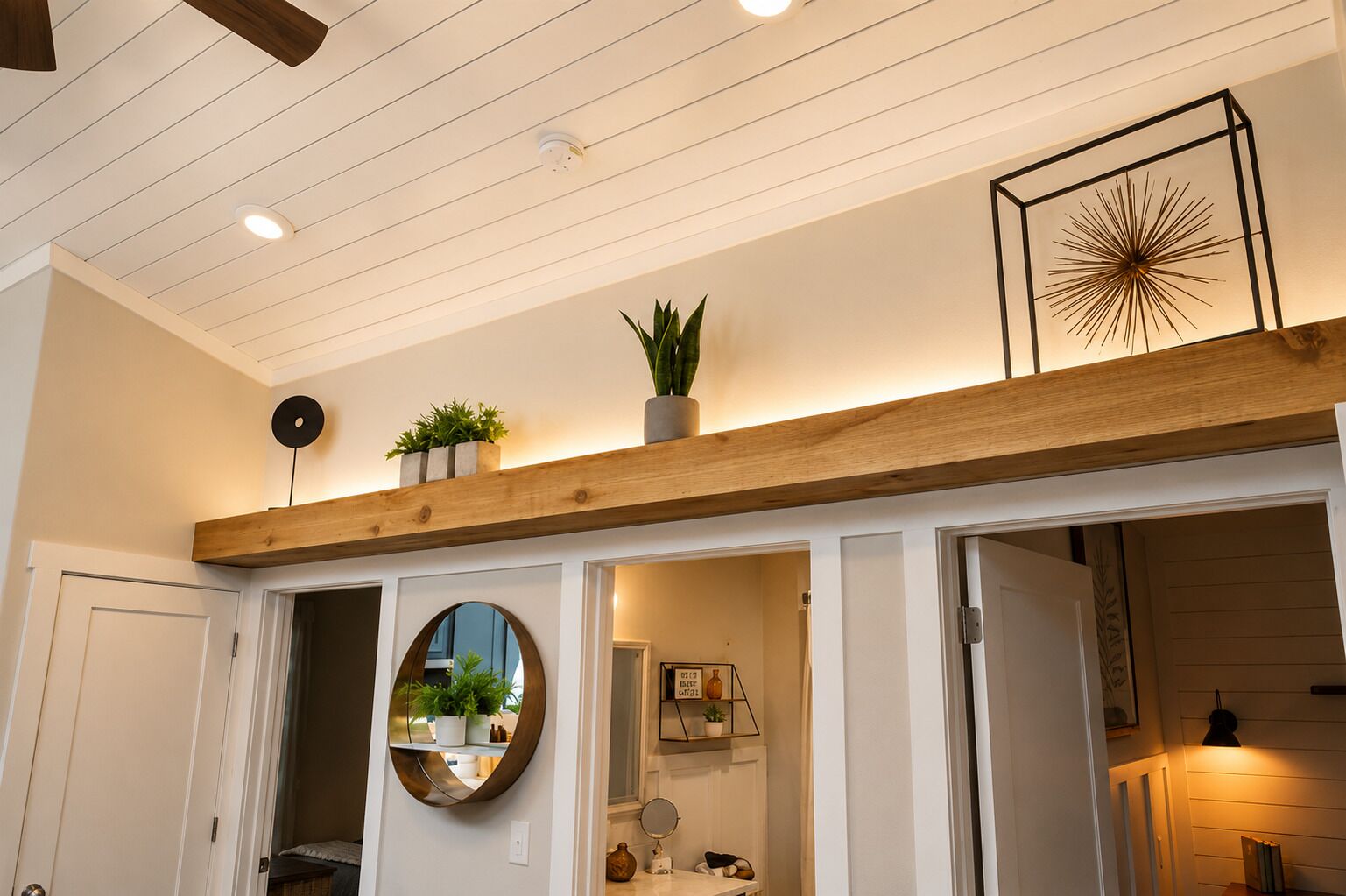 A hallway with a wooden beam ceiling, a round mirror, and a framed artwork.
