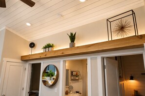 Un couloir avec un plafond orné de poutres en bois, un miroir rond et une œuvre d’art encadrée.