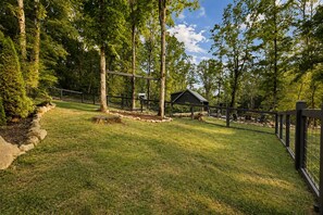 A fenced outdoor area with a small building, surrounded by trees and grass.