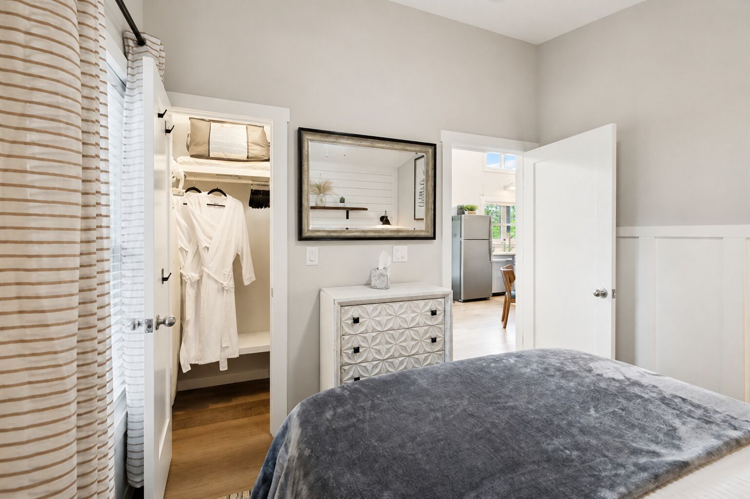 A bedroom with a bed, a dresser, a mirror, and a closet with hanging robes.
