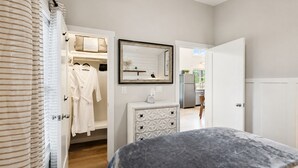 Un dormitorio con cama, cómoda, espejo y armario con batas colgadas.