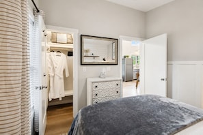 A bedroom with a bed, a dresser, a mirror, and a closet with hanging robes.