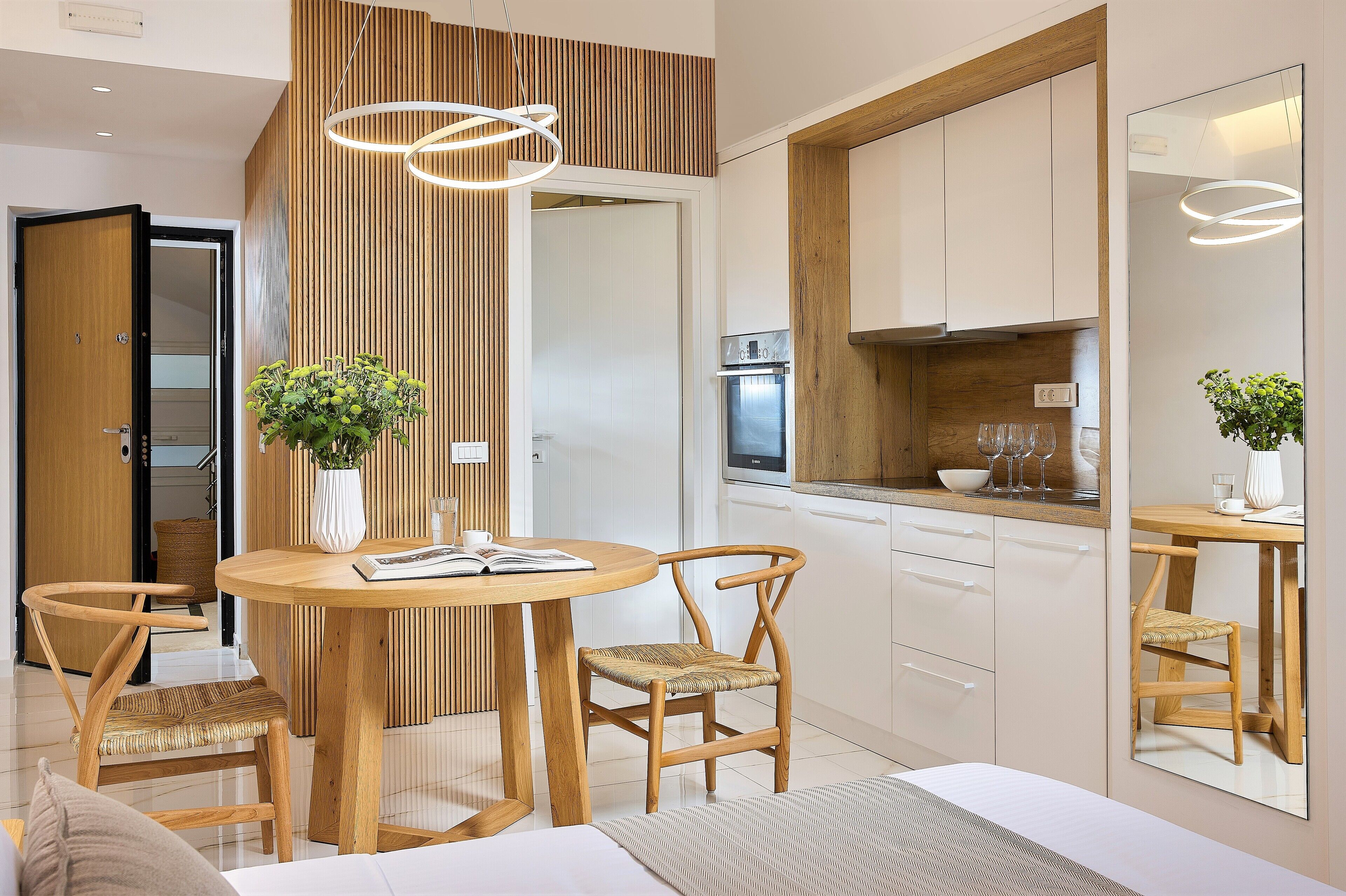 A modern kitchen with wooden cabinetry, a built-in oven, and a dining area with a round table and two chairs.