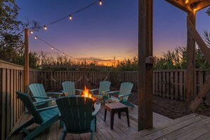 A deck with chairs and a fire pit, surrounded by a wooden fence and string lights.