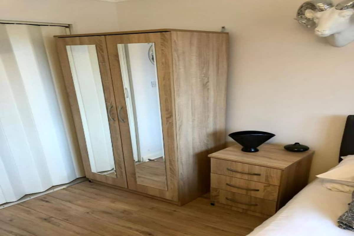 A bedroom with a wooden wardrobe, a bedside table with a lamp, and a bed with a white headboard.