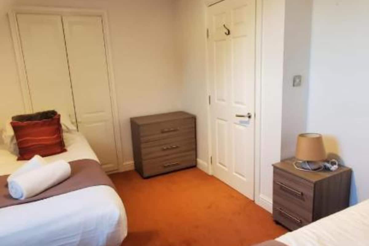 A hotel room with two beds, a dresser, a lamp, and a door.