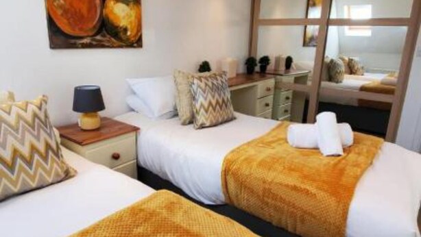 Ein Hotelzimmer mit zwei Betten, einem Bild an der Wand, einem Schreibtisch und einem Fenster.