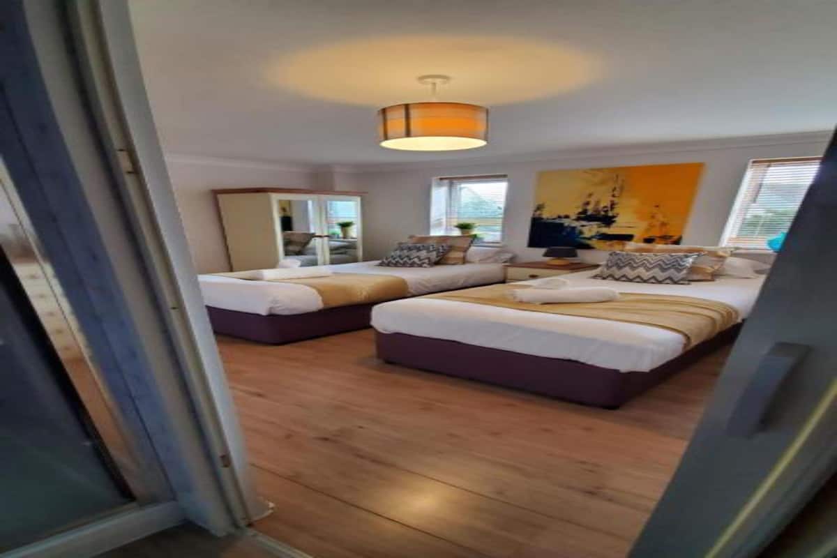 A bedroom with two beds, wooden flooring, a large window, and a ceiling light fixture.