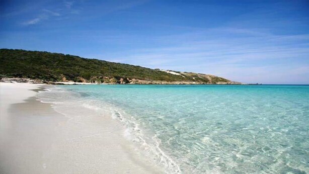 Una spiaggia con acque turchesi cristalline e sabbia bianca, circondata da colline verdi.