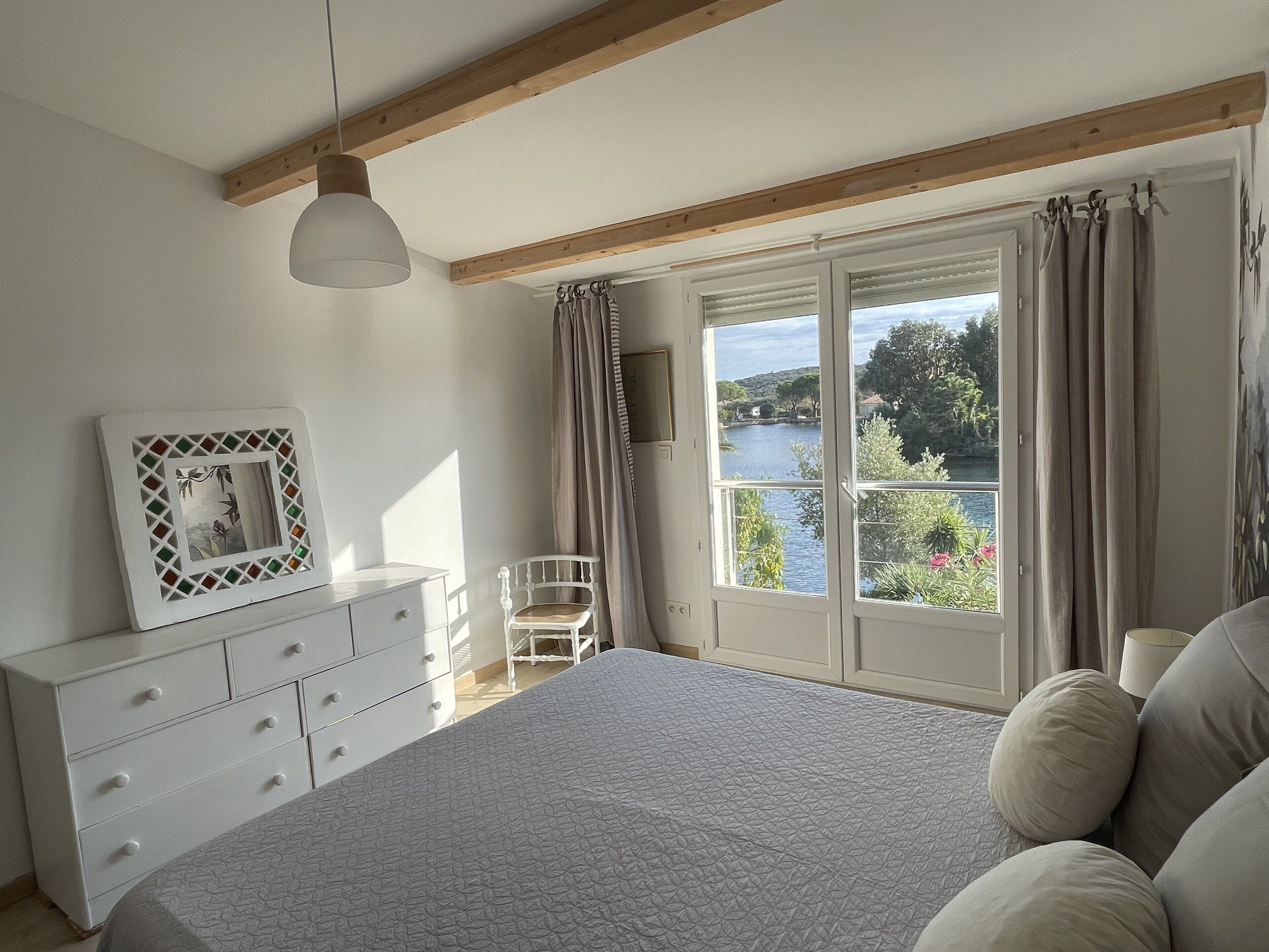 Un dormitorio con una cama grande, un aparador, una silla y una ventana con vistas a un lago.