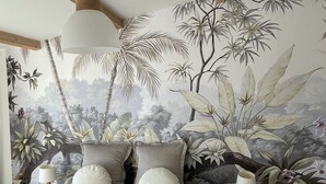 Una camera da letto con un letto grande, due lampade da comodino e un murale a tema tropicale sulla parete.