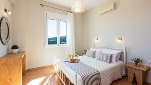 Une chambre à coucher comprenant un lit, des tables de chevet, une fenêtre avec des rideaux, un appareil de climatisation et une vue sur l’extérieur.