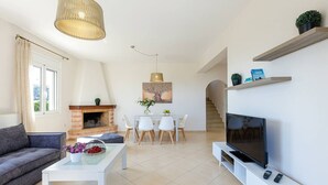Un salon moderne comprenant un canapé, une table basse, un téléviseur, une cheminée, un coin repas et un escalier.