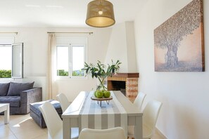 A dining area with a table, chairs, a vase with flowers, a fireplace, and a painting on the wall.