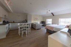 A modern kitchen with white cabinets, a dining area with a white table and chairs, a grey sofa, and a large window providing natural light. - Apartment 9 Isabella House Hereford (Hereford)