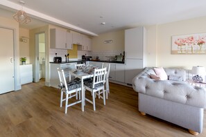 A modern kitchen with white cabinets, a dining table with chairs, and a grey sofa in a living area. - Apartment 9 Isabella House Hereford (Hereford)
