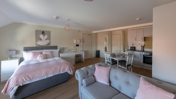 Una camera da letto moderna con un letto grande, un divano grigio e una zona pranzo con una cucina sullo sfondo.