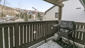 A balcony with a barbecue grill, a wooden fence, and a view of a snowy landscape and buildings in the background. - C305 W Beaver Creek Blvd 2 Bedroom Condo by RedAwning (Avon)