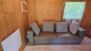 A wooden interior with a sofa and striped pillows, a white radiator, and a window with a view of trees. - Eastern Nostalgia in the Cabin Village (exclusive use) - Yacht tour starting at 7 days, booking included (Groß Köris)