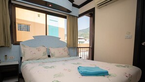 A bedroom with a bed, a nightstand, a window with curtains, and a view of buildings outside. - Phuket Paradise Hotel (Patong)
