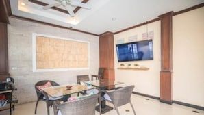 A dining area with a glass table and wicker chairs, a television on the wall, and a large map artwork. - Phuket Paradise Hotel (Patong)