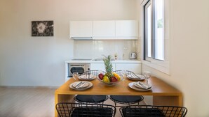 A modern kitchen with white cabinets, a wooden dining table set for four, and a fruit bowl on the table.
