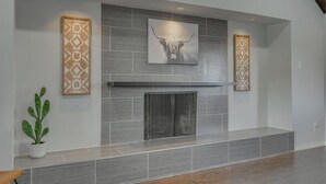A modern fireplace with a geometric patterned wall above it, a framed artwork of a bull's head, and a potted plant to the left. - Dream Vacation Home with Pool for Large Groups! (Garland)