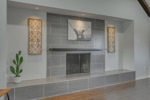 A modern fireplace with a geometric patterned wall above it, a framed artwork of a bull's head, and a potted plant to the left. - Dream Vacation Home with Pool for Large Groups! (Garland)