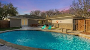 A backyard with a swimming pool, two lounge chairs, a covered patio, and a wooden fence. - Dream Vacation Home with Pool for Large Groups! (Garland)