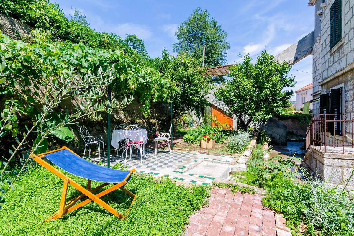A garden with a checkered patio, outdoor seating, and a small stream.