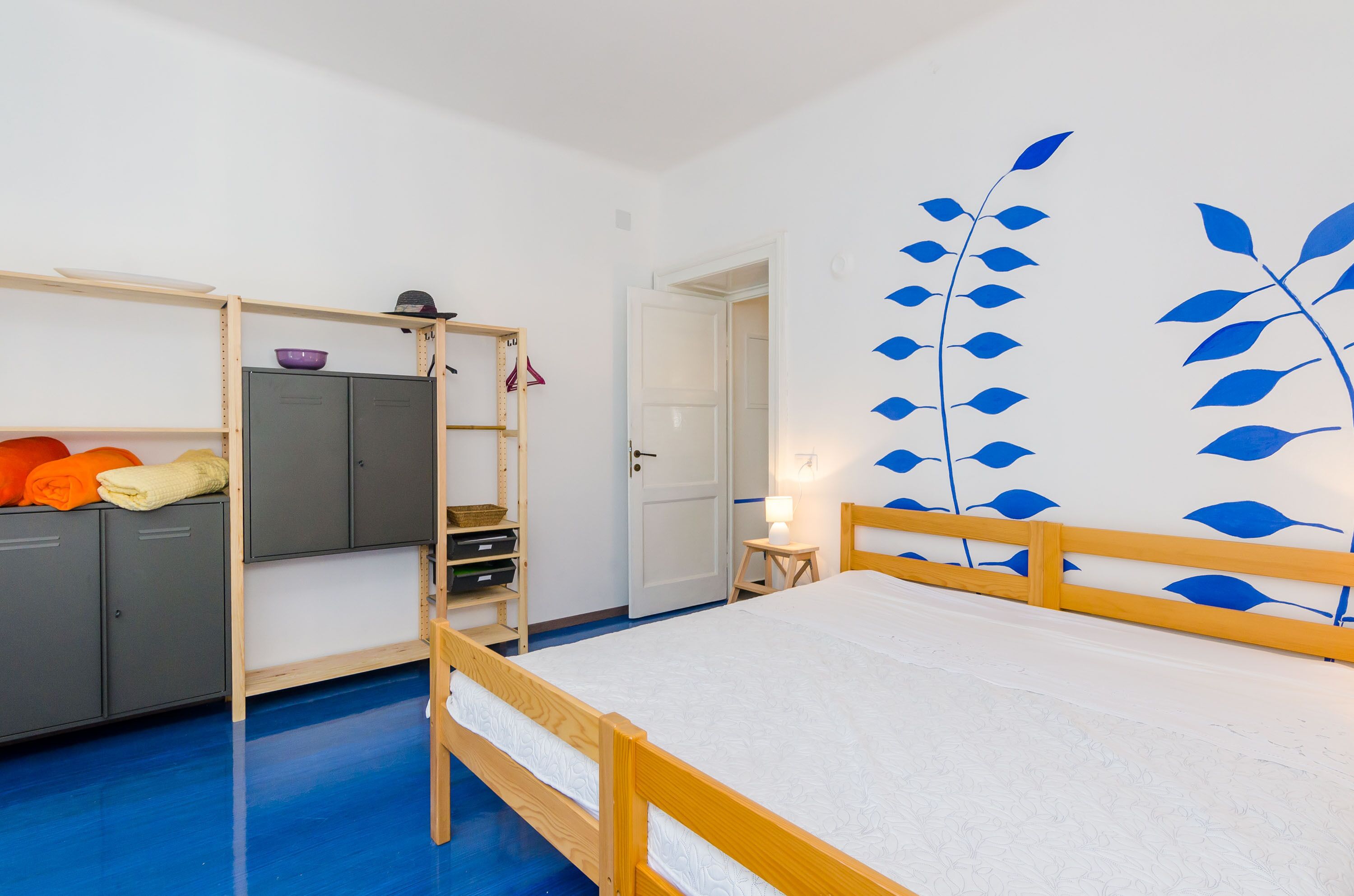 A room with a bunk bed, a wardrobe, a small table with a lamp, and a wall with a leaf pattern.