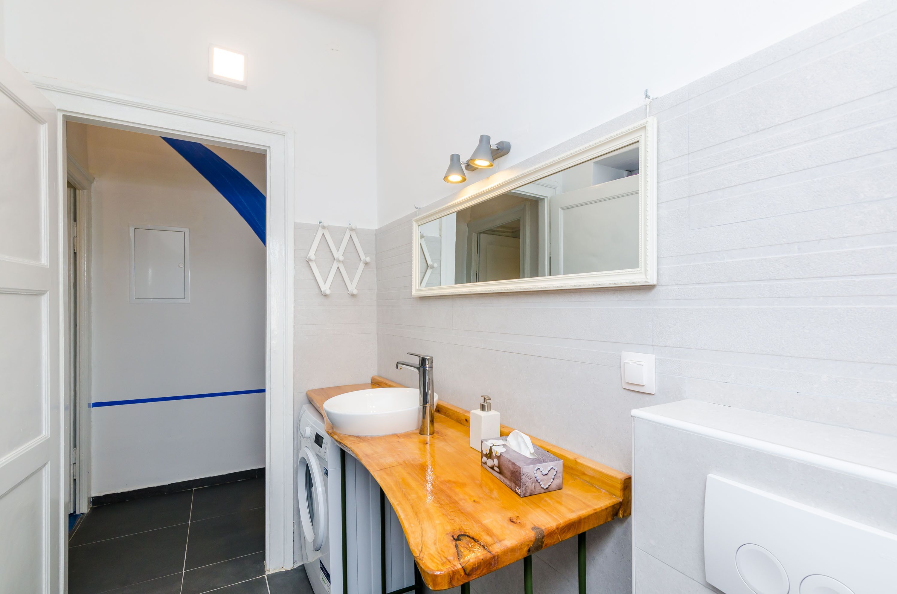 A bathroom with a wooden vanity, a white sink, a mirror, and a washing machine.
