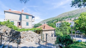 A stone staircase leading to a building with a red-tiled roof, surrounded by greenery and a hillside village in the background. - Apartments Eos & Vespera (Dubrovnik)