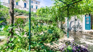 A garden with a pergola, a stone building, and a blue door. - Apartments Eos & Vespera (Dubrovnik)
