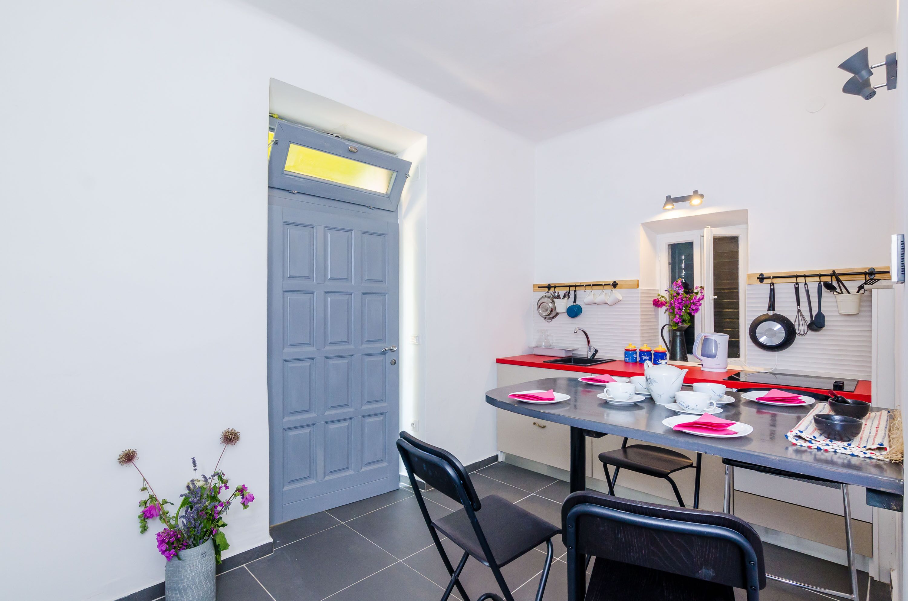 A compact kitchen with a dining table set for four, a blue door, and a small flower arrangement.