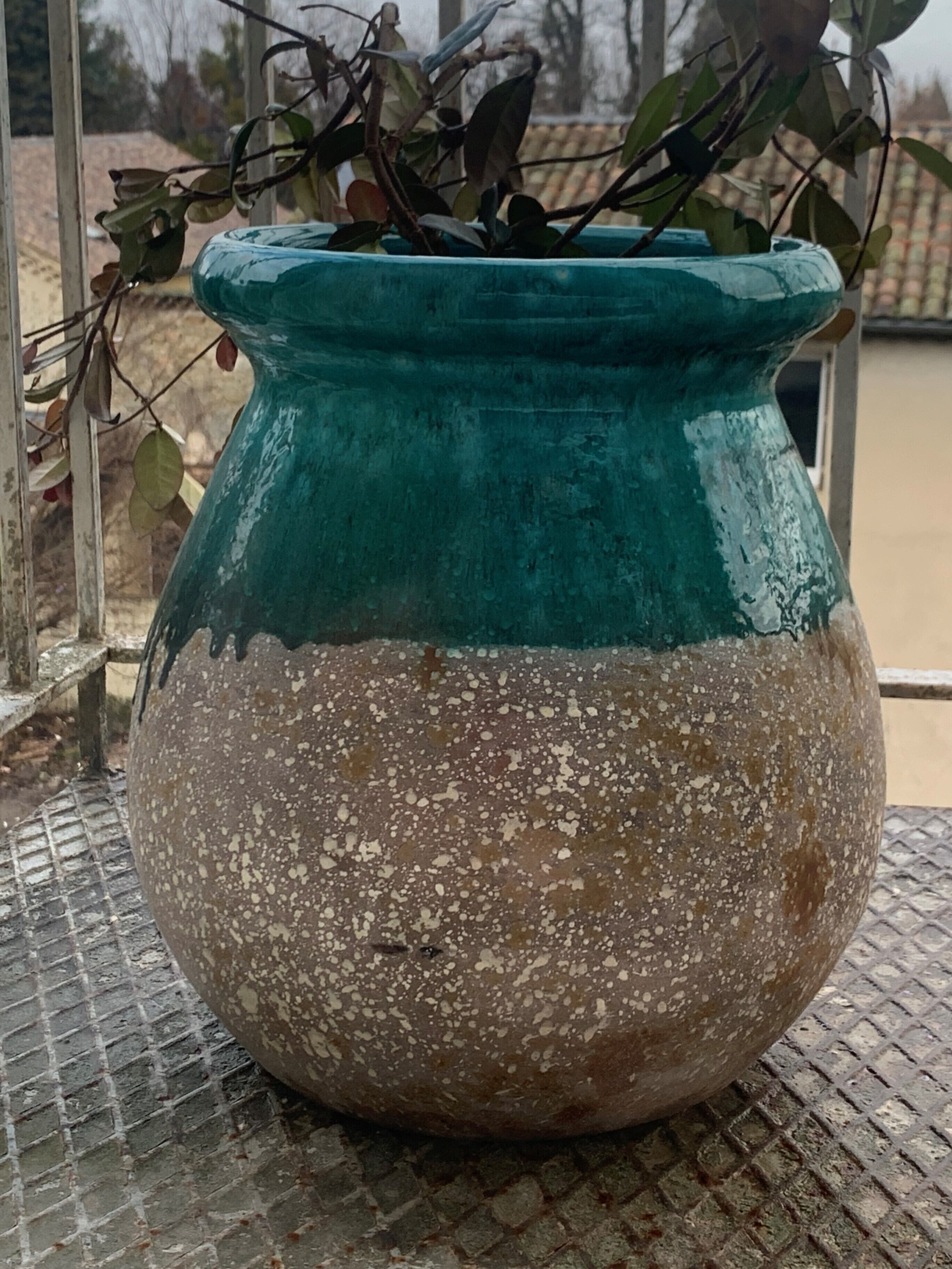 A large, speckled ceramic pot with a teal upper section, placed on a metal grate.