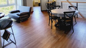 Un vaste espace de vie comprenant un canapé, une table à manger et des chaises. Une grande fenêtre offre une belle vue sur la nature et permet à la lumière naturelle d’entrer.