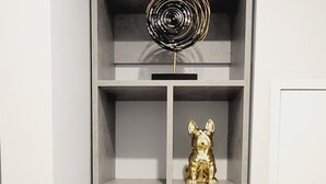 Une étagère grise sur laquelle sont posés un objet décoratif en métal, une statuette de chien dorée et plusieurs plantes en pot.